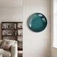 Genesis Jade 3D Resin Crystal Porcelain LED Wall Art by Giant Sculptures, glossy jade-green disc mounted on a cream wall beside a walnut bookshelf and sofa.