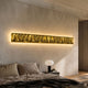 Textura 3D Gold Leather Design Wall Art by Giant Sculptures, a long horizontal panel with sculpted gold relief, backlit above a bed beside a globe lamp.