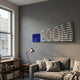 Illustra Deep Blue Highlight BOOM Text 3D Wooden Wall Art by Giant Sculptures, displayed in a grey living room above a sofa beside a window and desk lamp.