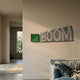 Illustra Teal Highlight BOOM Text 3D Wooden Wall Art mounted on a beige living room wall beside a green square accent, above a blue linen sofa.
