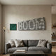 Illustra Green Highlight BOOM Text 3D Wooden Wall Art by Giant Sculptures above a grey sofa, paired with a small green textured square piece and floor lamp.