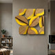 Lignos Yellow Accent Wooden Leaf Motif 3D Wall Art mounted on a grey wall in a modern living room with a bookshelf, potted plant, and fireplace nearby.