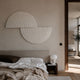Orbitals White Semi-Circle Wood Carved Sandstone 3D Wall Art by Giant Sculptures mounted above an upholstered bed with linen bedding in a warm minimalist bedroom.