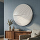 Orbitals White Circular Wood Carved Sandstone 3D Wall Art by Giant Sculptures mounted above a walnut sideboard with vases and eucalyptus against a blue wall.