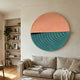 Orbitals Peach & Teal Circular Wood Carved Sandstone 3D Wall Art mounted above a linen sofa in a Nordic living room with bookshelves and a plant.