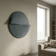 Orbitals Deep Teal Circular Wood Carved Sandstone 3D Wall Art by Giant Sculptures mounted on a textured beige wall beside a tall window and linen sofa.