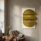 Ellipse Gold Oval Wood 3D Canvas Wall Art by Giant Sculptures displayed in a sunlit corner above a mid-century armchair, brass desk lamp, and small plant.