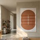Ellipse Terracotta Oval Wood 3D Canvas Wall Art by Giant Sculptures displayed on a beige wall in a sunlit Nordic-style hallway with a bookshelf nearby.