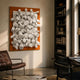 Axion White Wood Cluster & Burnished Orange Edge 3D Wall Art mounted in a sunlit living room above a brown leather chair, beside a dark bookshelf.