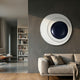 Aetherial Midnight Blue Glossy Circular Asymmetry 3D Wall Art by Giant Sculptures mounted on a dark grey wall above a beige sofa in a modern living room.