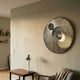 Orbitra Gold Reflective Circular 3D Wall Art by Giant Sculptures mounted above a wooden side table with lamp in a warm neutral living room.