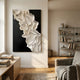 Stratura IV Black & White Layered Paper Canvas Wall Art by Giant Sculptures displayed in a neutral living room above a wood console with books and a bookshelf.