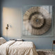 Oculis Earthy Balance Square Handmade 3D Paper Wall Art by Giant Sculptures, beige metallic sunburst in a clear acrylic frame, mounted above a linen bed.