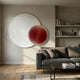 Lucentis White & Burgundy Wood Relief 3D Wall Art by Giant Sculptures, a wavy white disc overlapping a burgundy lined circle, above a grey sofa.