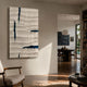 Striata White & Blue Wood Carving 3D Wall Art by Giant Sculptures mounted in a sunlit modern living room with a wooden armchair and dining area beyond.
