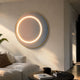 Aurora Blush Mist Crystal Porcelain LED Wall Art mounted above a white sofa, its glowing warm-white ring illuminating the pink and blue gradient within a slim gold frame.