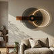 Eclipse II Charcoal Bronze Acrylic 3D LED Wall Art by Giant Sculptures mounted above a beige sofa, with glowing arc, dark circle and wooden bar composition.