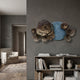 Luminis Bloom Blue Floral Metal Wall Art by Giant Sculptures mounted above a low bookshelf in a grey living room with armchair and rug nearby.