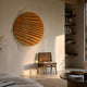 Auramesh Sunset Orange-I Metal Winged Circular Geometric Wall Art by Giant Sculptures displayed above a cane chair in a warm-toned living room with bookshelves.