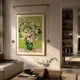 Reverra White Blossoms Hanging Frame Wall Art by Giant Sculptures, white florals in a green vase with gold frame and tassels, above a sofa in a sunlit living room.