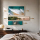 Visario Ocean & Nature Inspired Metal Wall Art by Giant Sculptures, three gold-framed panels showing surf, coastal landscape, and turquoise water, displayed above a dark wood console in a bedroom.