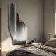 Celestial Flow Waterfall curved metal wall art in glossy black, white, and grey mounted above a bedside table in a neutral bedroom beside the bed.
