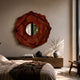 Sculptura Mirror Terracotta Red Floral Round Metal Wall Art hung above a wooden sideboard in a modern bedroom with vases, books, and soft natural light.