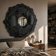 Sculptura Mirror Charcoal Grey Floral Round Metal Wall Art with layered petals and open centre, mounted above a bed beside a mushroom lamp and nightstand.