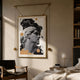 Eterna Classics David Replica wall art in a gold frame with rod-and-weight suspension, hung above a chair and bed in a warm bedroom.