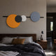 Orbit III Radiant Balance Multicoloured Circular Wall Art by Giant Sculptures, with orange, black, white, and blue-grey discs on a black bar above a bedroom.