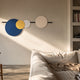 Orbit I Radiant Balance wall art by Giant Sculptures with navy, yellow, grey, and beige discs on a black line above a cream sofa in a sunlit living room.