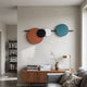 Orbit II Radiant Balance wall art by Giant Sculptures with orange, black, white, and teal discs on a black bar, mounted above a walnut sideboard in a living room.