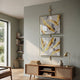 Vortice Feather Elegance Dual Panel Wall Art by Giant Sculptures, two stacked square panels with gold and silver feathers in a slim brass frame, displayed above a cane sideboard in a sage living room.
