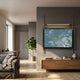 Celestique Golden Pavilion Framed LED Wall Art by Giant Sculptures mounted on a grey wall above a wooden console in a modern living room with sofa and fiddle-leaf fig.