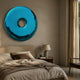 Auro Sapphire Blue Round Gloss Metal 3D Wall Art by Giant Sculptures mounted above an upholstered bed in a neutral bedroom with a stone lamp and linen drapes.