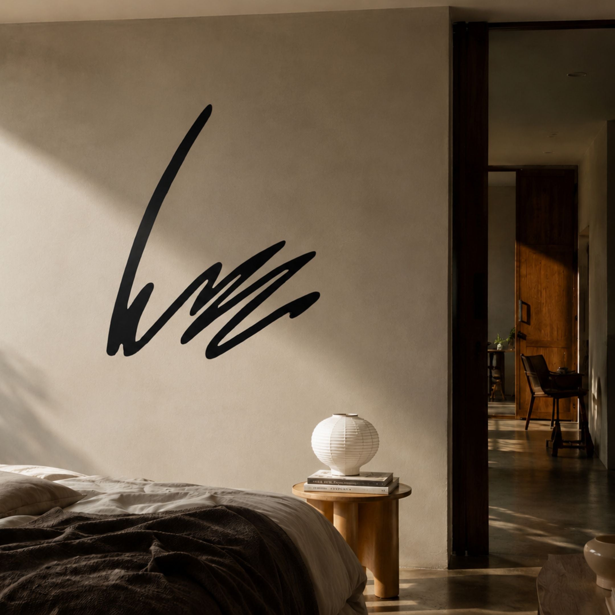 Oscura Ripple Effect Black Abstract Metal Wall Art mounted on a cream bedroom wall above a wooden side table holding a white paper lantern and books.