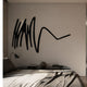 Oscura Dynamic Flow Black Abstract Metal Wall Art by Giant Sculptures mounted above a bedroom console with books, vase, and lamp beside a linen-dressed bed.