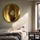 Auro Gold Round Gloss Metal 3D Wall Art by Giant Sculptures, a mirror-polished gold ring sculpture mounted above an upholstered bed in a sunlit bedroom.