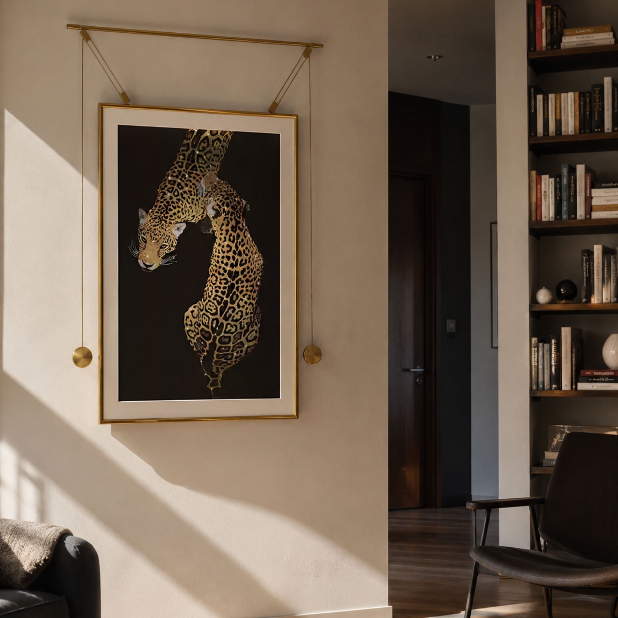 Glacia Dual Jaguar Crystal Hanging Framed Wall Art by Giant Sculptures in a gold steel frame with suspended weights, displayed on a beige wall beside a bookshelf.