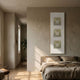 Lustre Golden Illusion Plaster Statue Vertical Wall Art by Giant Sculptures displayed above a linen bed in a warm neutral bedroom with hallway view.
