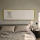 Lustreline White Left Plaster Statue Cardboard Wall Art by Giant Sculptures in a thin gold frame above a grey linen bed with bedside table and lamp.