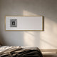 Lustreline Black & White Left Plaster Statue Cardboard Wall Art in a slim gold frame, displayed above a bed with linen bedding in a sunlit bedroom.