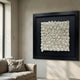 Harmonia 3D Spiral Ceramic Wall Sculpture with black frame displayed above a beige sofa in a sunlit minimalist living room with pale plaster walls.