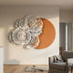 Fleur Halo Terracotta wall art by Giant Sculptures with white metal flowers layered over a terracotta-orange disc, mounted in a neutral living room above a grey armchair.