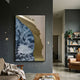 Astrid Azure Flow Gold Abstract Wall Art by Giant Sculptures hung on a dark grey wall in a living room with armchairs and a bookshelf nearby.