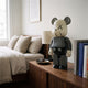 X-Mark Studio Grey Bear Sculpture - 70cm in grey and black resin on a walnut nightstand beside books and a lamp in a bedroom setting.