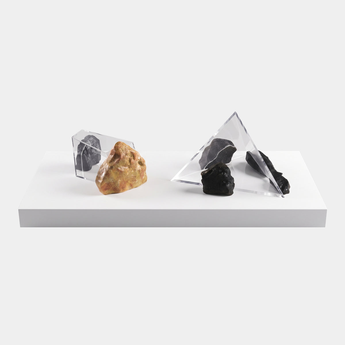 Clear Acrylic Prisms with Printed Stone on Marble Base - 170cm, showing a triangular prism with a rust-brown stone and a tetrahedron with dark grey stones on a long white marble base, plain light background.