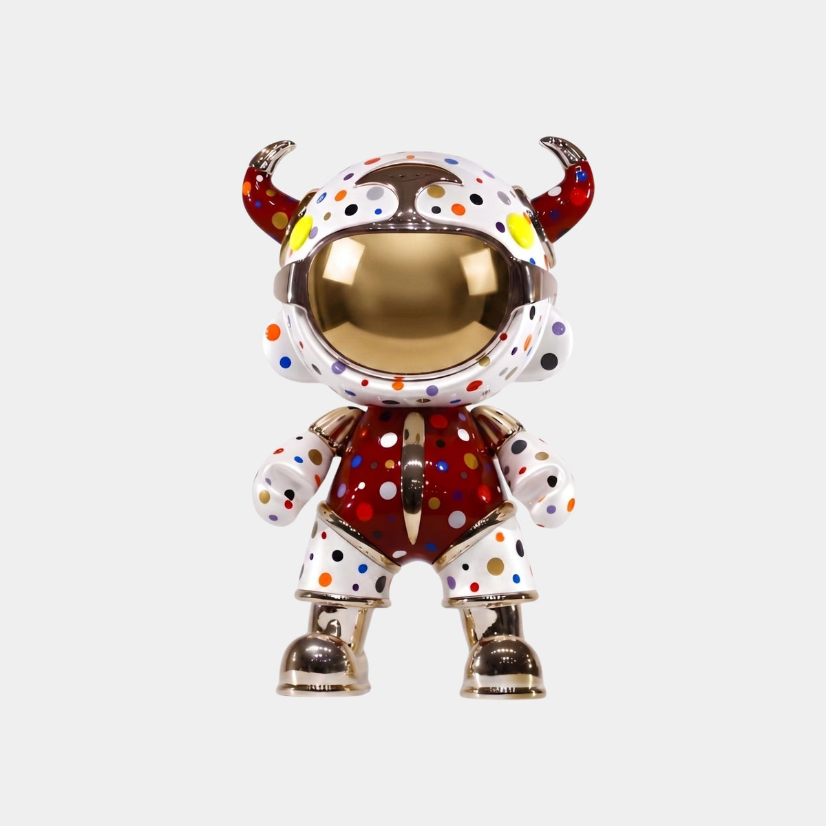 The Giant Sculptures Crimson Confetti Suit Astro Devil Figure (48cm) features a horned helmet, metallic gold accents, and mirrored visor. Its red body with white panels and colorful polka dots creates a playful pop-art look against a white background.