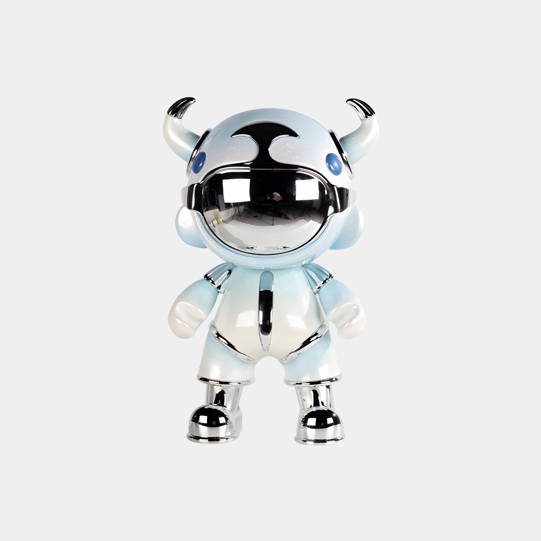 The Sky Blue Suit Astro Devil Figure by Giant Sculptures is a 48cm metallic designer sculpture with a round head, horns, and chrome visor, resembling a robot or astronaut in light blue and silver against a white background.