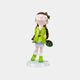 The Meadow Green Lulabelle Sculpture - 60cm by Giant Sculptures depicts a joyful girl in a green jacket and boots with a striped bag, head tilted back, all elegantly crafted on a white base.